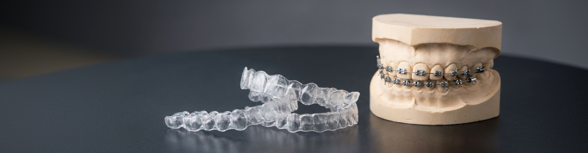 Pair of clear aligners beside mouth model with metal braces.2